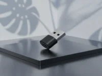 Adaptador USB Tipo-C para Tipo-A equilibrado em plataforma metálica sob sombras de folhas tropicais.
