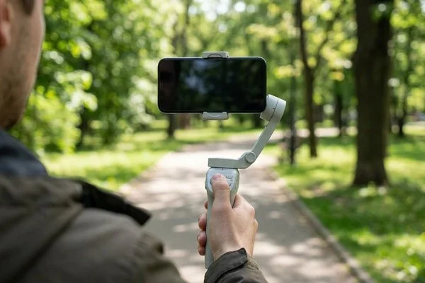 Ilustração de pessoa de costas em um parque, segurando um celular de tela apagada em um estabilizador de mão